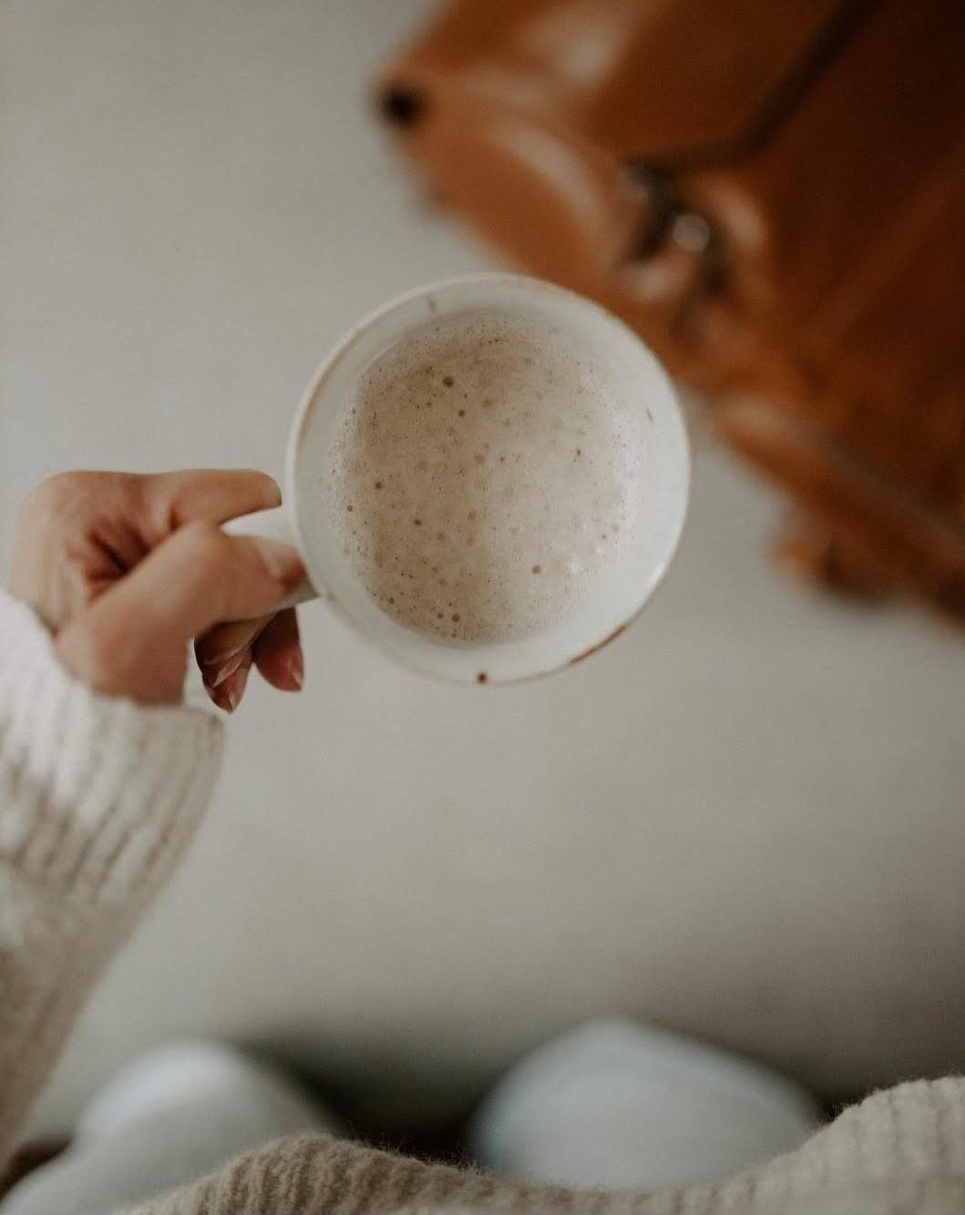 Woman wearing cozy clothes and holding a cup of cocoa with an Native Soul Trading Co bag in the background. 